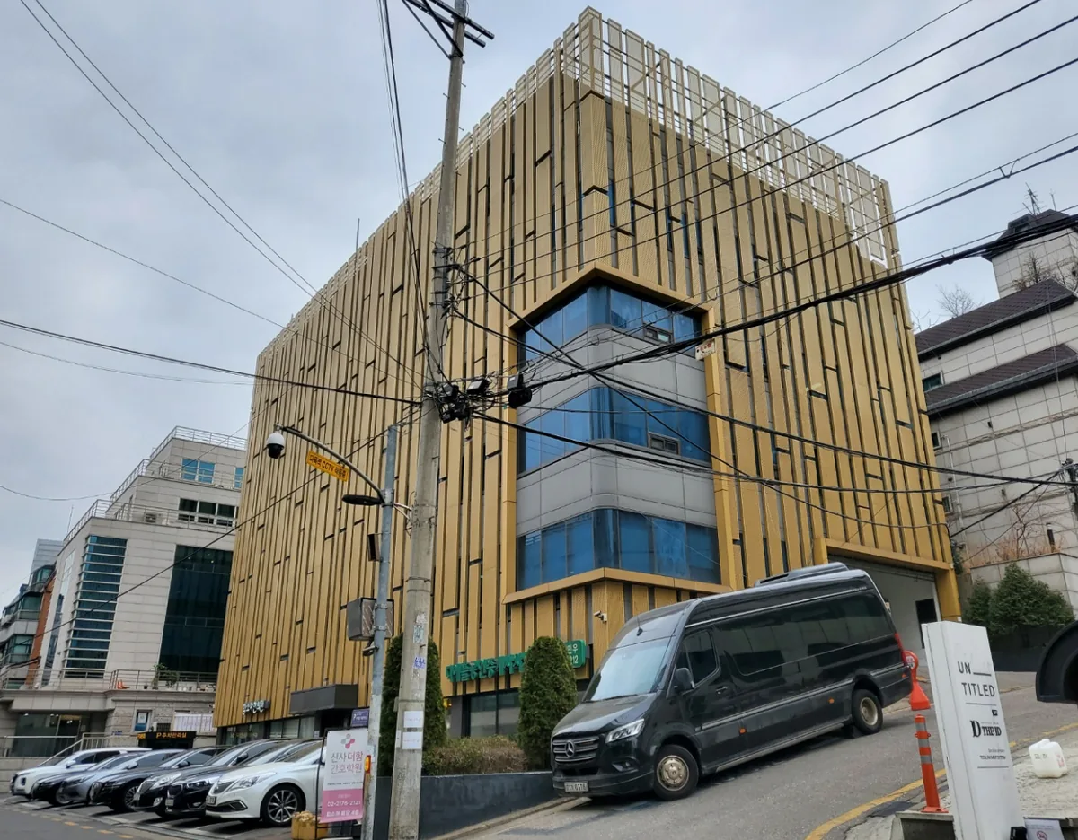 논현동 10-26 코너 외관 – 금색 세로 루버 사이로 유리 커튼월이 드러나는 6층 빌딩