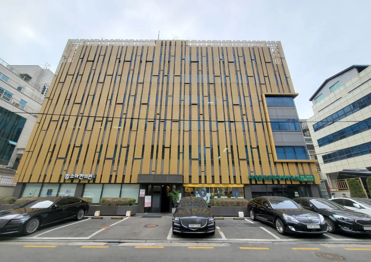 논현동 10-26 정면 – 1층 한의원과 카페가 들어선 금색 루버 파사드와 전면 주차장
